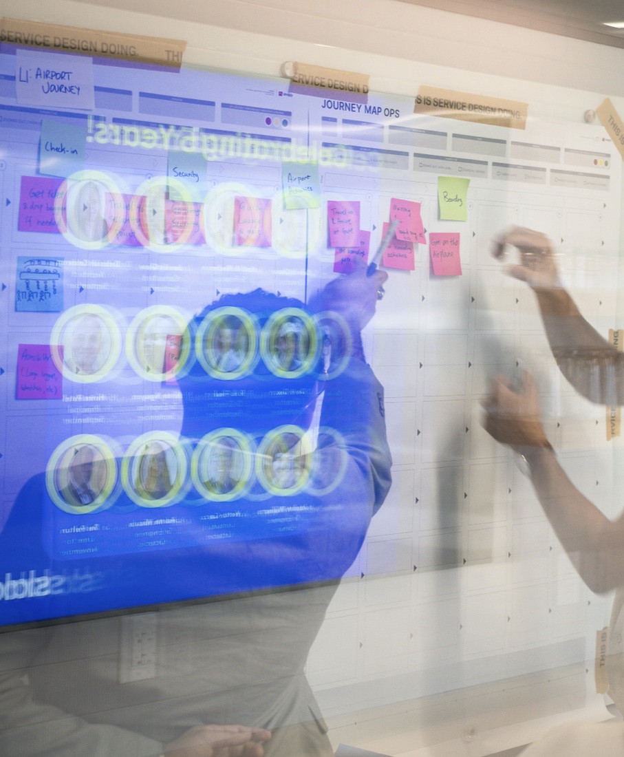 A participant adding ideas to a journey map, photographed through glass